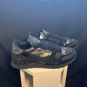 Valentino Rockrunner i camouflage - Snygga Valentino Rockrunner sneakers i svart och grått med ett coolt camouflage-mönster. Skorna har snörning och är tillverkade i en kombination av mocka och syntetmaterial. Perfekta för en stilren look. Äkta såklart, skicket är som nya. Kan gå ned i pris vid snabb affär