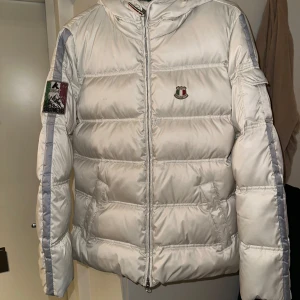 Vit dunjacka från Dolomite - Säljer en snygg vit dunjacka från Dolomite med broderad logga på ryggen och en liten patch på ärmen. Jackan har en dragkedja framtill och är långärmad. Perfekt för kyliga dagar med sin pufferdesign som håller dig varm.