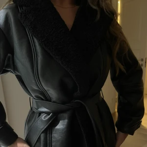 VIRAL slutsåld Svart skinnjacka med bälte från h&m  - Snygg svart skinnjacka ifrån hm! krage i pälsimitation. Jackan har ett bälte i midjan för en justerbar passform och långa ärmar med stiliga detaljer. Storlek M, vart slutsåld ett tag och gått viralt! Säljer pga att jag ej använt! HELT NY med prislapp på