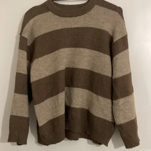 Brun och beige randig tröja - Säljer en mysig brun och beige randig tröja med långa ärmar. Perfekt för kyligare dagar med sin avslappnade passform och ribbade detaljer vid hals, ärmslut och nederkant.