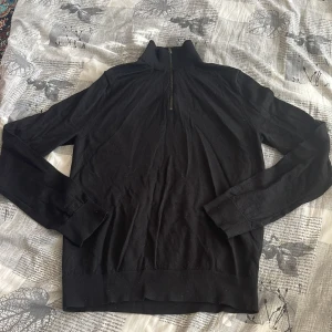 Svart långärmad tröja med dragkedja från H&M - Säljer en stilren svart långärmad tröja med dragkedja vid halsen. Perfekt för kyligare dagar och enkel att matcha med olika outfits. Strynklig men ordnars med att bara stryka det. 