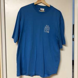 Säljer en blå t-shirt med ett litet tryck på bröstet. T-shirten har en rund hals och korta ärmar. Perfekt för en avslappnad stil.