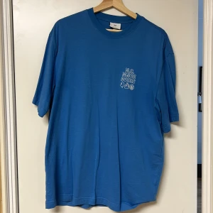 Blå t-shirt med tryck - Säljer en blå t-shirt med ett litet tryck på bröstet. T-shirten har en rund hals och korta ärmar. Perfekt för en avslappnad stil.