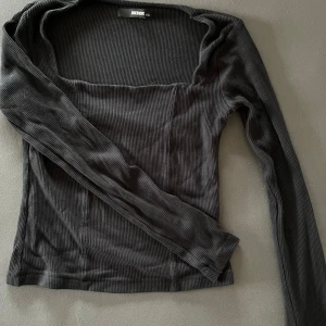 Svart ribbad topp från BikBok - Säljer en stilren svart ribbad topp från BikBok med långärmad design och fyrkantig halsringning. Perfekt för en chic och enkel look. Passar bra till både jeans och kjol.
