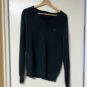 Mörkblå v-ringad tröja från Gant - Snygg mörkblå v-ringad tröja från Gant med broderad logga på bröstet. Tröjan har långa ärmar och ribbade kanter vid ärmslut och nederkant. Perfekt för en stilren look.