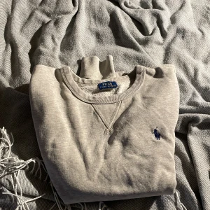 Grå tröja från Polo Ralph Lauren - Säljer en stilren grå tröja från Polo Ralph Lauren med rund halsringning och det klassiska logotypbroderiet på bröstet. Perfekt för en avslappnad look. Tröjan har långa ärmar och ribbade muddar.