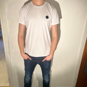  T-shirt Moncler - En snygg vit T-shirt från Moncler med ett snyggt tryck på baksidan. Storleken är Medium. Hör av dig vid funderingar!
