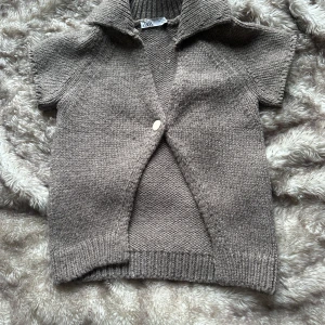 Beige stickad kofta från Zara - Säljer en mysig beige stickad kofta från Zara med korta ärmar och en knapp framtill . en ribbad krage som ger en stilren look. 