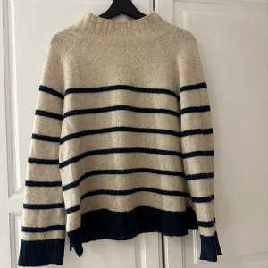 Beige randig tröja från Hampton Republic - Säljer en snygg beige tröja från Hampton Republic med mörkblå ränder. Tröjan har en hög krage och långa ärmar, perfekt för kyligare dagar. Den är tillverkad i ett mjukt material som ger en skön känsla. Passar utmärkt till både jeans och kjol.