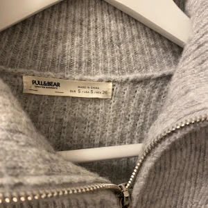 Grå stickad tröja från Pull&Bear - Mysig grå stickad tröja från Pull&Bear med dragkedja framtill, stl S.
