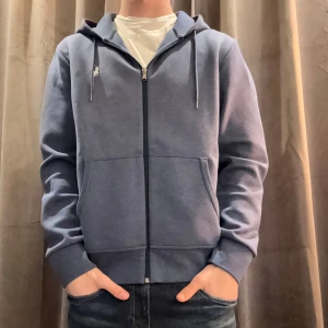 Blå hoodie från Ralph Lauren - Säljer en stilren blå hoodie från Ralph Lauren med dragkedja och justerbar huva. Tröjan har långa ärmar och en liten broderad logotyp på bröstet. Perfekt för en avslappnad look.