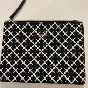 Svartvit kuvertväska från Malene Birger - Snygg kuvertväska från Malene Birger i svartvitt mönster. Väskan har en praktisk dragkedja och ett stilrent mönster som ger en elegant touch. Perfekt för att bära med sig det nödvändigaste.