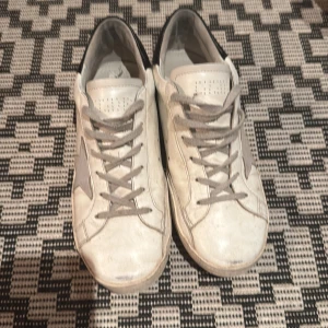 Golden goose - Snygga vita sneakers från Golden Goose med grå stjärndetalj på sidan och grå snörning. Skorna har en svart häl och perforerade detaljer på tån. Perfekta för en avslappnad stil. Pris kan diskuteras.