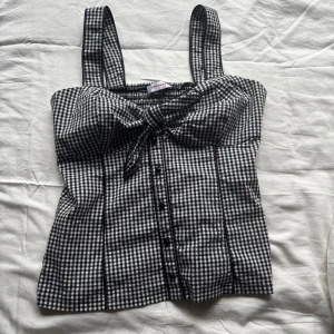 Korsettopp - Säljer en snygg svartvit rutig korsettopp från Orsay. Den har knappar och rosett fram och är smockad i ryggen. Står ingen storlek men skulle säga typ M 🩷