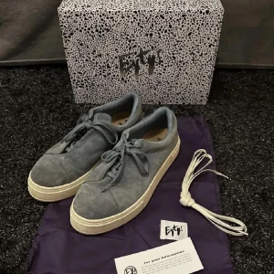 Grå sneakers från Eytys - Snygga grå sneakers från Eytys i mocka med vit sula. Skorna har en stilren design med en mörk lila detalj på hälen. Perfekta för en avslappnad stil. Låda tillkommer inte