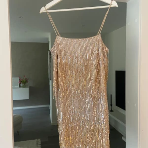 Glittrig guldklänning med paljetter - Säljer en fantastisk glittrig guldklänning från hm Klänningen är täckt med paljetter och har smala axelband. Perfekt för att glänsa på festen! ✨Helt oanvänd