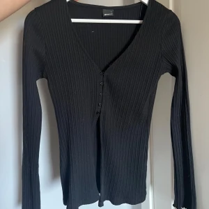 Svart ribbad tröja från Gina Tricot - Säljer denna snygga svart ribbad tröja med knappar i fram från Gina Tricot. Eftersom att den aldrig har använts 