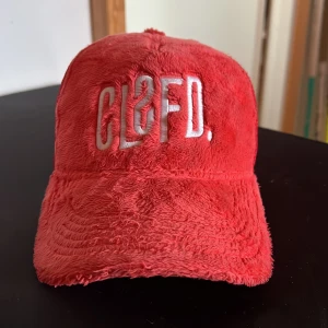 Röd keps från Classified - Snygg röd keps med pälsig textur och broderad logga framtill.  Baksidan har ett justerbart nät för perfekt passform. Perfekt för att sticka ut med stil.     Pris:249         Nypris: 599