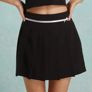 Svart kjol  - Söt svart kjol med en vit dekorativ rosett och band i midjan. Aldrig använd pga för liten. Skriv om du vill ha mått eller har några funderingar 💕