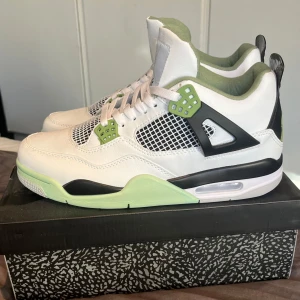 Jordan 4 seafoam - Snygga Nike Air Jordans i vitt med gröna och svarta detaljer. Skorna har en klassisk design med snörning och synlig luftdämpning i sulan. Perfekta för dig som vill ha en stilren och sportig look.
