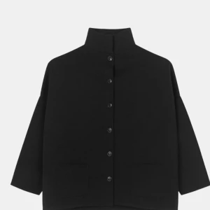 Svart kappa med knappar - Snygg svart kofta med hög krage och knappar framtill. Den har en minimalistisk design med rakan linjer och trekvartsärmar. Perfekt för en stilren look.