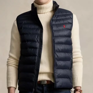 Mörkblå dunväst från Ralph Lauren - Snygg mörkblå dunväst från Ralph Lauren med dragkedja och broderad logga på bröstet. Perfekt för lager-på-lager under kyliga dagar.