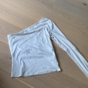 Vit oneshoulder topp från H&M - Säljer en stilren vit oneshoulder topp från H&M. Den är långärmad och passar perfekt till allt. Materialet är mjukt och bekvämt. Jag säljer den eftersom den inte passar längre.