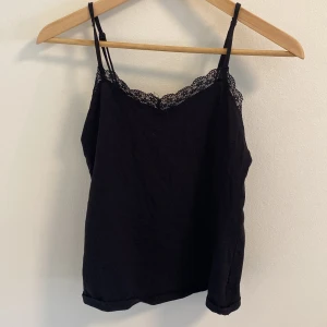 Svart linne med spetsdetaljer från H&M - Säljer ett svart linne från H&M i storlek S. Det är ärmlöst med smala axelband och har fina spetsdetaljer längs halsringningen. Perfekt för både vardag och fest!