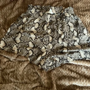 Ormmönstrade shorts - Säljer ett par coola ormmönstrade shorts i storlek 36. De är perfekta för en somrig dag eller en utekväll. Shortsen har en elastisk midja för extra komfort och är gjorda i ett mjukt material som känns skönt mot huden. Mönstret är riktigt trendigt och ger en edgy look!