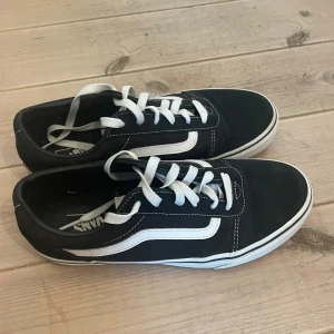 Svarta sneakers från Vans - Säljer ett par klassiska svarta Vans sneakers med vit sula och den ikoniska vita sidostripen. Skorna har snörning och är i bra skick. Perfekta för vardagsbruk och ger en skön streetstyle-look.