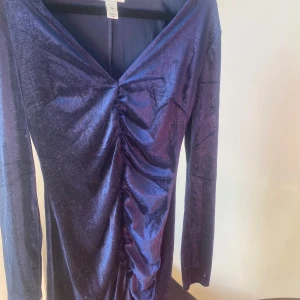 Mörkblå glittrig klänning - Säljer en superfin mörkblå klänning med glittrigt material. Den har en snygg v-ringad design och långa ärmar. Klänningen har en cool rynkad detalj framtill som ger den en unik look. Perfekt för fest eller nyår!