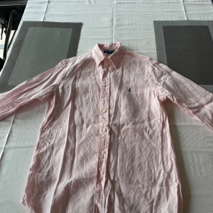 Ralph Lauren skjorta  - Säljer en snygg rosa skjorta från Ralph Lauren i storlek S. Skjortan är långärmad och har en klassisk krage med knappar. Den är tillverkad i ett mjukt bomullsmaterial och har en broderad logga. Skriv vid minsta lilla funderingar 