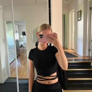 Svart kortärmad topp med knytband - Säljer en snygg svart topp med korta ärmar och coola knytband runt midjan. Perfekt för en utekväll eller fest! Toppen är tight och ger en stilren look.