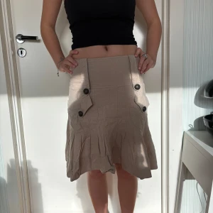 Medellång kjol  - Beige kjol som går ner till knäna. Lågmidjad kjol med knappar. Säljer pågrund av liten användning. Jättebra skick!