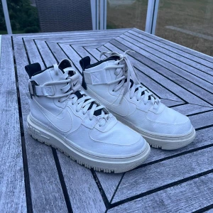 Vita Nike Air Force sneakers - Säljer ett par vita Nike Air Force sneakers i bra skick. De har en hög modell med snörning och en cool remdetalj runt ankeln. Skorna har en robust sula och är perfekta för både vardag och fest. De är bekväma och stilrena, ett måste i garderoben! Inköpt på Nike hösten 2023, i MOS. Kom privat för mer bilder eller info.