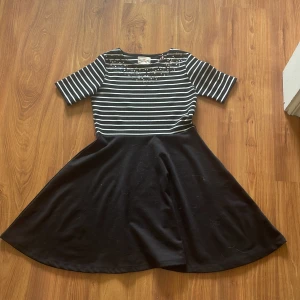 Randig klänning från Holly & Whyte - Säljer en superfin klänning från Holly & Whyte by Lindex eftersom den inte passar mig längre. Den har en randig överdel i svart och vitt med glitter på överdelen. Klänningen är bara använde ett fåtal gånger så den är i väldigt bra skick.