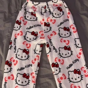 Hello Kitty mjukisbyxor - Supermysiga populära vita mjukisbyxor med Hello Kitty-motiv över hela tyget. Byxorna har ett gulligt mönster med röda rosetter och Hello Kittys ansikte. Perfekta för en chill dag hemma eller som pyjamasbyxor. De är gjorda i ett mjukt och bekvämt material som känns skönt mot huden. 💕💕 