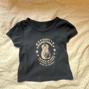 Brandy Melville topp  - Säljer en cool svart t-shirt med Nashville-tryck och en gitarr i mitten.  Toppen är använt ett fåtal gånger🩷skulle tippa att den passar XS-S i storlek 