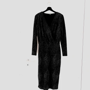 Svart glittrig klänning från Esprit - Säljer en superfin svart klänning från Esprit. Den är glittrig och perfekt för festliga tillfällen. Klänningen har en omlott-design med långärmade ärmar och en v-ringad hals. Materialet känns lyxigt och den sitter riktigt snyggt på kroppen. Perfekt för nyår eller en utekväll! Använd 1 gång. Frakt tillkommer.