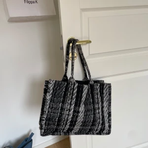 Svartvit rutig väska från H&M - Säljer en snygg svartvit rutig väska från H&M. Perfekt för att bära med sig allt man behöver under dagen. Väskan har ett stilrent mönster och är rymlig med bekväma handtag. Den är i bra skick och redo för nya äventyr!