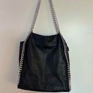 Svart Tiamo Väska - Säljer denna supersnygga väskan från Tiamo eftersom den aldrig kom till användning! Jättebra skick, använd 1-2 gånger bara. Stor modell med mycket utrymme, perfekt till skolan! 💞 Den har flera fack inuti, och även ett fack på baksidan.