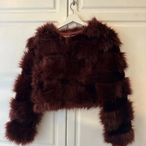 Brun pälsjacka från PrettyLittleThing - Säljer en supercool brun pälsjacka från PrettyLittleThing. Den är croppad och har långa ärmar, perfekt för att göra ett statement i höst och vinter. Jackan är i syntetmaterial och känns riktigt lyxig och mysig. Perfekt för fest eller en utekväll! 🐻✨
