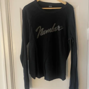 Svart långärmad tröja från Number (N)ine - Svart långärmad tröja från Number (N)ine. Den har en cool logga på framsidan i glittrigt material. 
