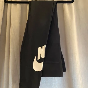 Svarta mjukisbyxor från Nike - Säljer ett par svarta tights från Nike. De är superbekväma och perfekta för chill eller träning. Byxorna har en stor vit Nike-logga på benet som ger en sportig look.