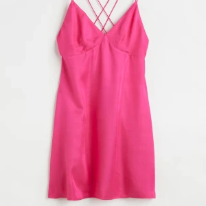 Rosa sidenklänning med korsade band - Säljer en superfin rosa klänning i satin med korsade band i ryggen. Den är ärmlös och har en smickrande passform som passar perfekt för festliga tillfällen. Klänningen har en dragkedja på sidan för enkel påklädning. Perfekt för sommarens alla fester! 💖Den är kort och aldrig använd!