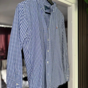 Blå och vit rutig skjorta från Polo Ralph Lauren - Säljer en snygg blå och vit rutig skjorta från Polo Ralph Lauren. Den har en slim fit passform och är långärmad. Skjortan är i bomull och har knappar framtill. Perfekt för både vardag och fest!
