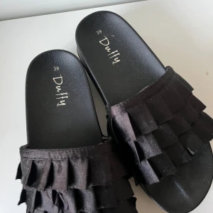 Svarta sandaler från Duffy - Säljer ett par snygga svarta sandaler från Duffy. De har en cool design med flera lager av volanger på ovansidan. Perfekta för sommaren och att glida runt i på stranden eller stan!