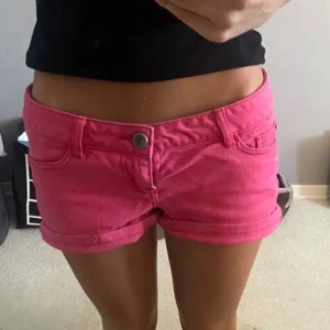 Rosa shorts - Snygga rosa shorts med låg midja och knappdetalj. Perfekta för sommardagar och avslappnade tillfällen. De har en klassisk design med fickor och är gjorda i ett bekvämt material.