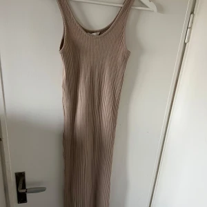 Beige ribbad långklänning - Säljer en stilren beige ribbad långklänning med ärmlös design. Klänningen har en smickrande passform och är gjord i ett mjukt material som känns skönt mot huden. Längd: vadlång.