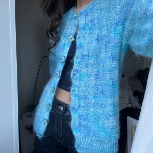 Blå stickad kofta med knappar - Säljer en mysig blå stickad kofta med unika knappar. Koftan har en härlig mix av blå nyanser och långa ärmar. Perfekt för kyligare dagar.